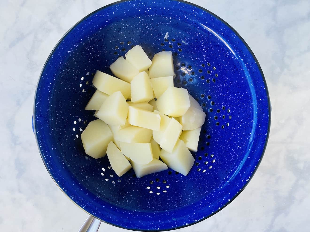 Boiled potatoes draining in a blue colander