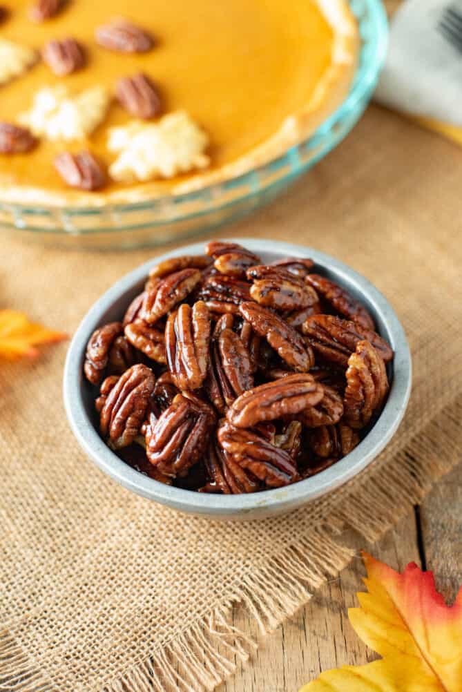 A grey bowl of glazed pecans with a sweet potato pie