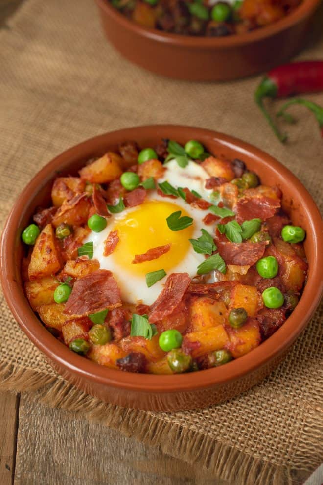 Huevos a la Flamenca (Gypsy Eggs)A terracotta bowl filled with potatoes, peas and chorizo in a tomat sauce topped with an egg