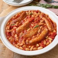 A round serving plate of Italian sausage and beans in a tomato sauce