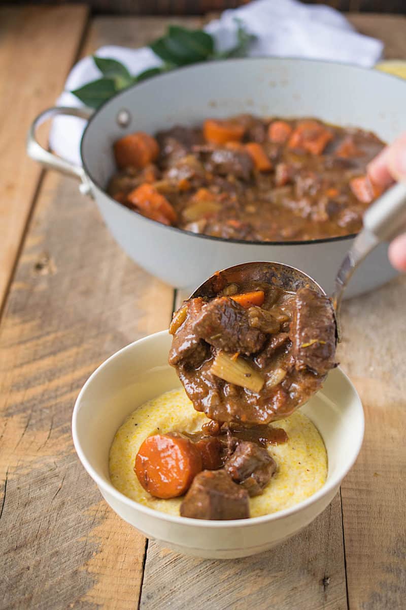 A ladle full of Italian beef stew being poured over polenta into a bowl