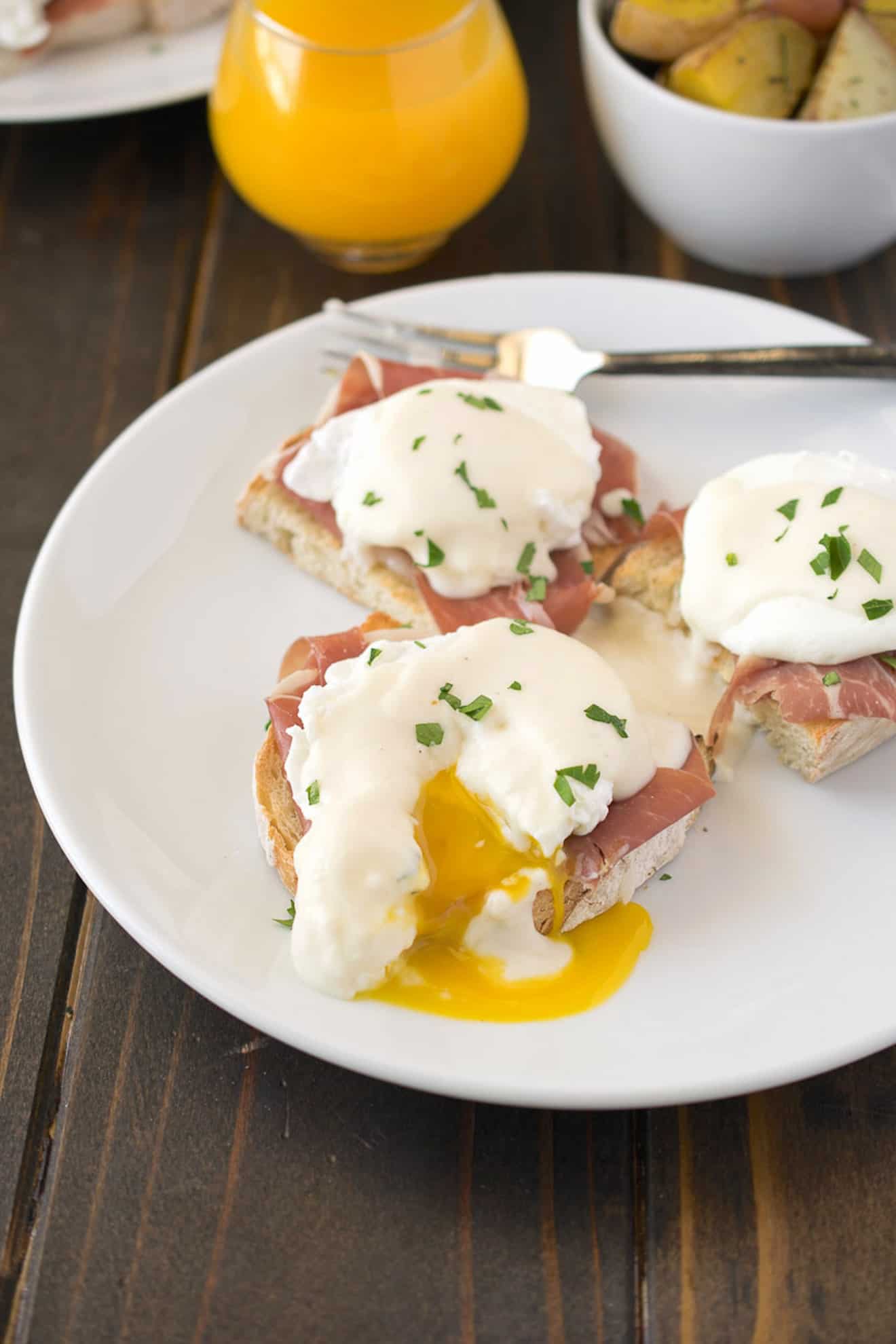 A poached egg on top of prosciutto and ciabatta bread cut open with yellow yolk running out