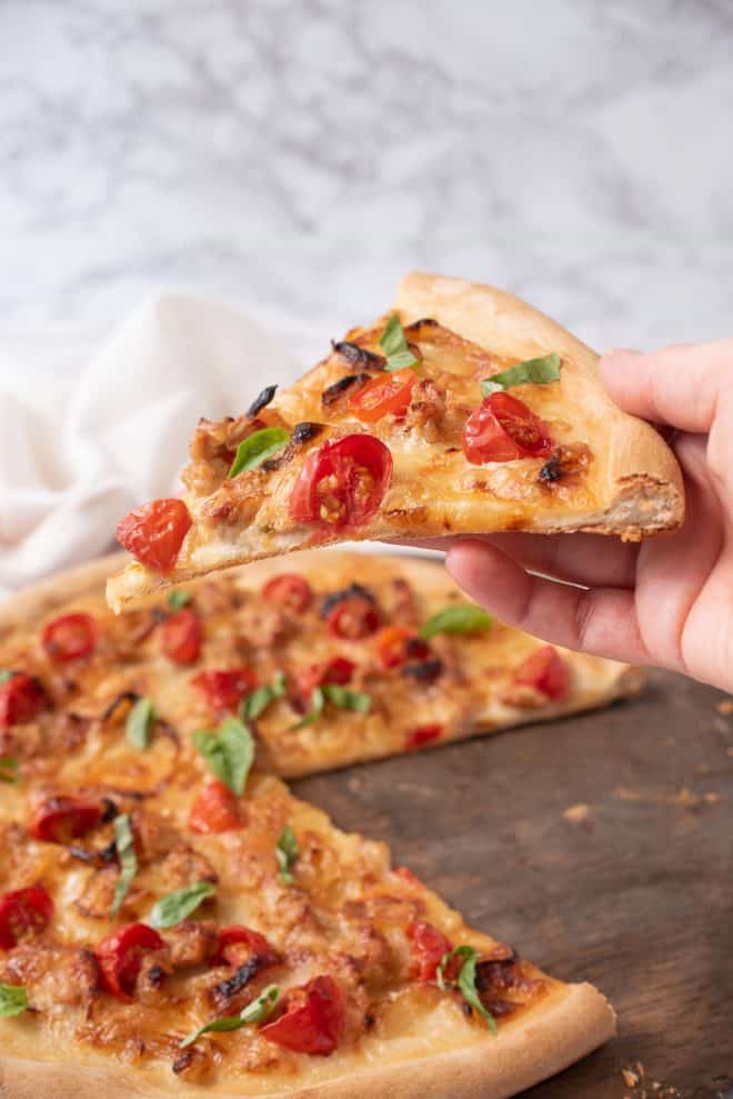 Holding a slice of Italian sausage and caramelized onion pizza