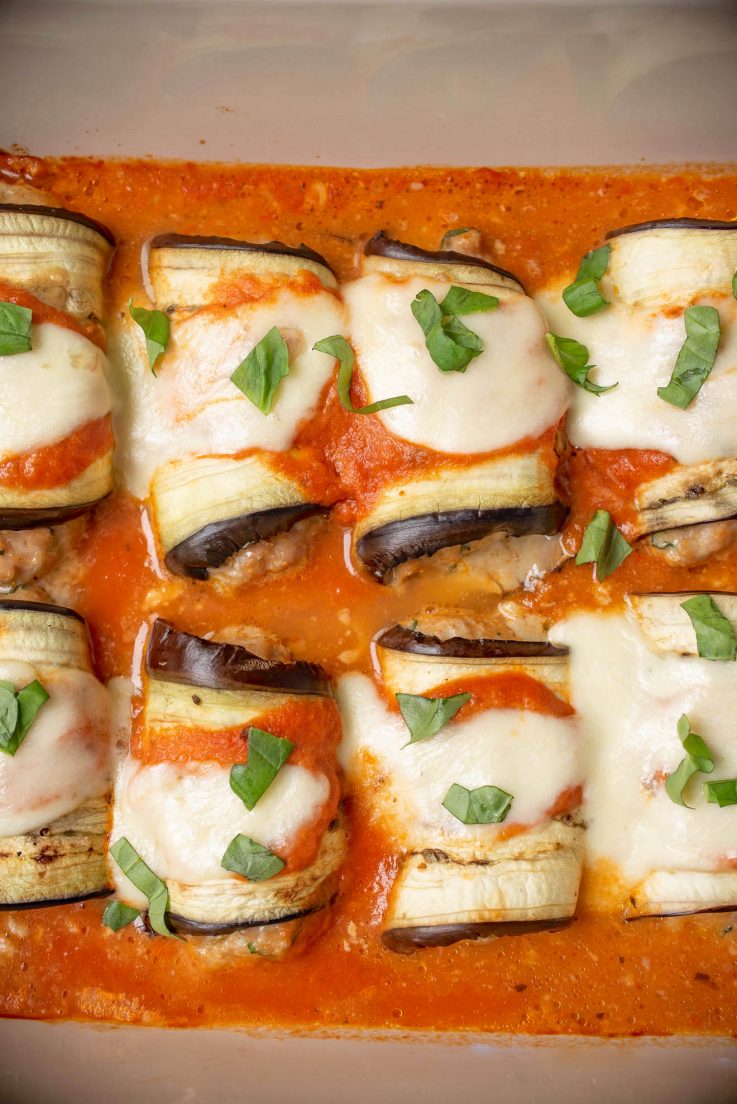 Eggplant rollatini in a baking dish topped with fresh basil
