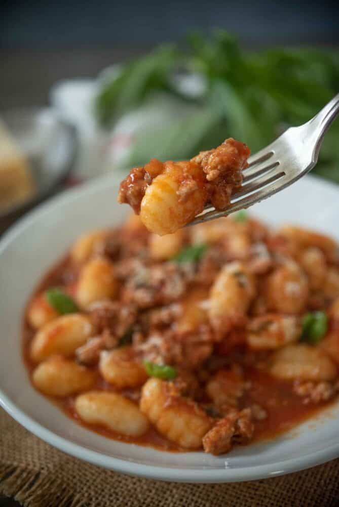 A piece of gnocchi on a fork with Italian sausage ragu.