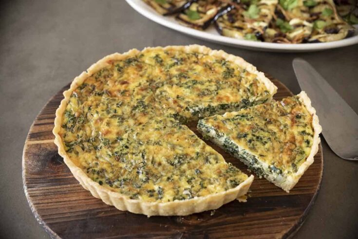 A spinach quiche on a round serving board with 1 cut piece