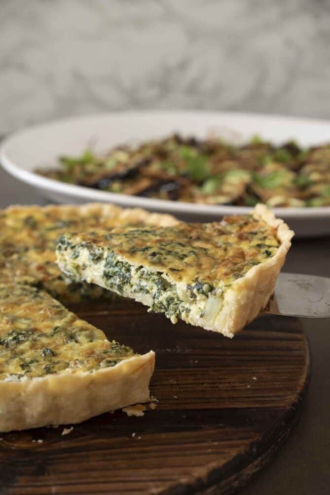 Lifting a slice of quiche showing the spinach in the filling