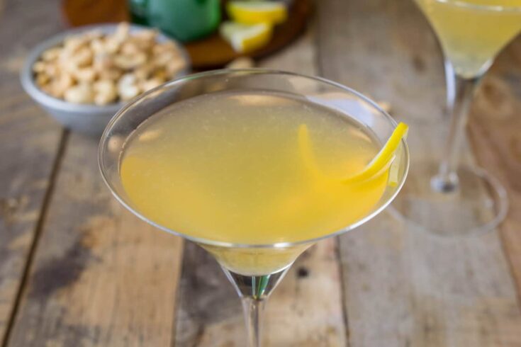 A closeup of a yellow cocktail with a twist of lemon rind