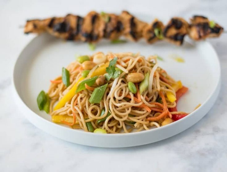 Noodle salad on a white plate with grilled chicken skewer