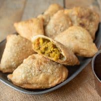 A cut open samosa showing the lentil curry filling laying on a plate with other samosa