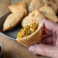 Holding a lentil samosa cut in half showing the filling