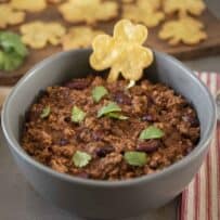 Meaty chili with beans in a grey bowl with a shamrock shaped tortilla chip