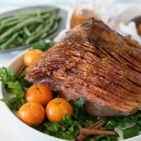 Mandarin Orange Spiced Glazed Ham presented and ready to serve on a bed of parsley with a side of green beans and sweet mashed potatoes