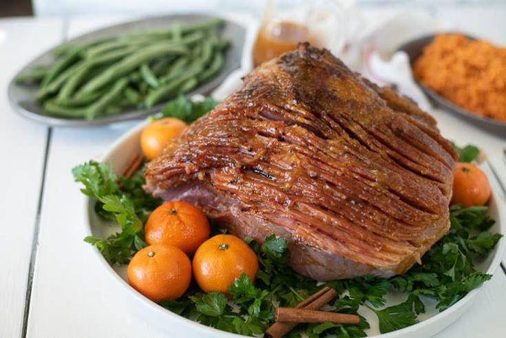 Mandarin Orange Spiced Glazed Ham presented and ready to serve on a bed of parsley with a side of green beans and sweet mashed potatoes