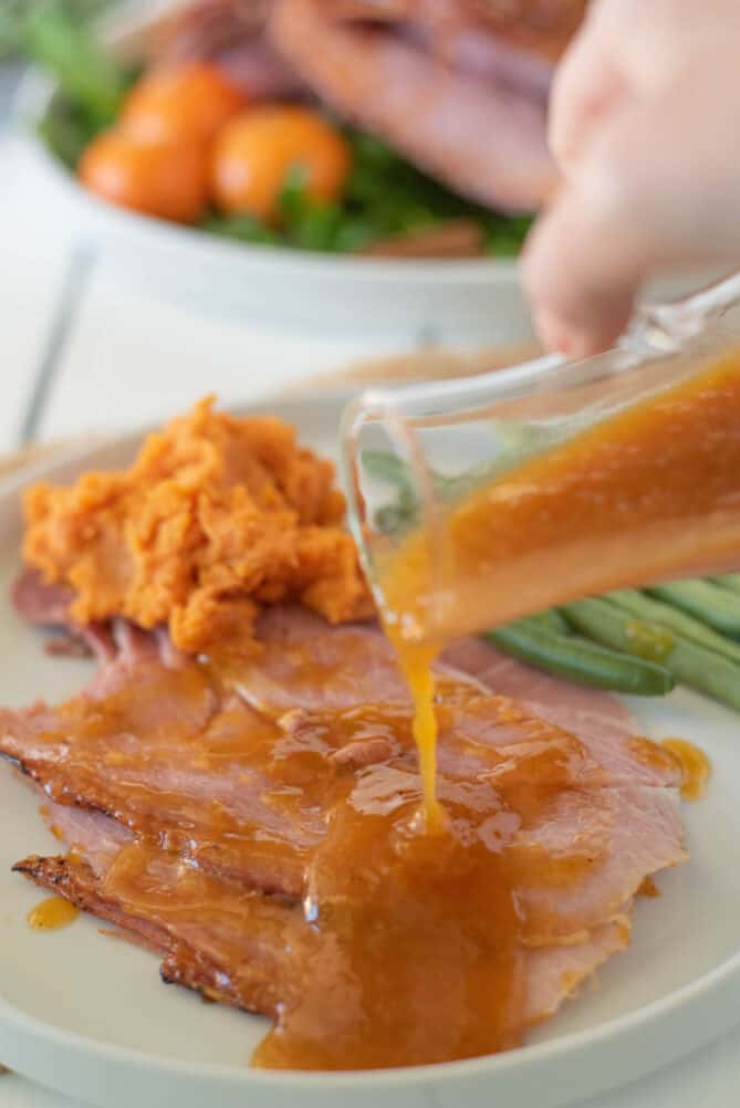 Pouring orange glaze over sliced ham
