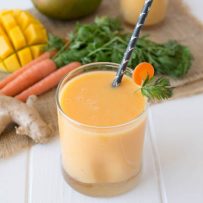 Smoothie in a short glass with a straw with fresh ginger, carrots and mango