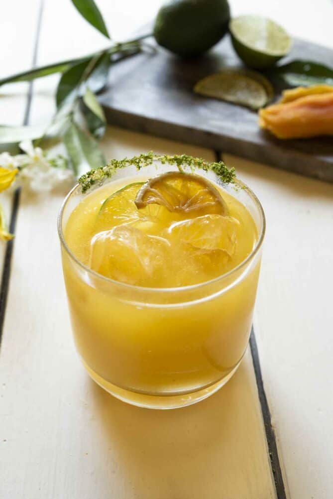 A mango mocktail in a short glass with a lime zest rim