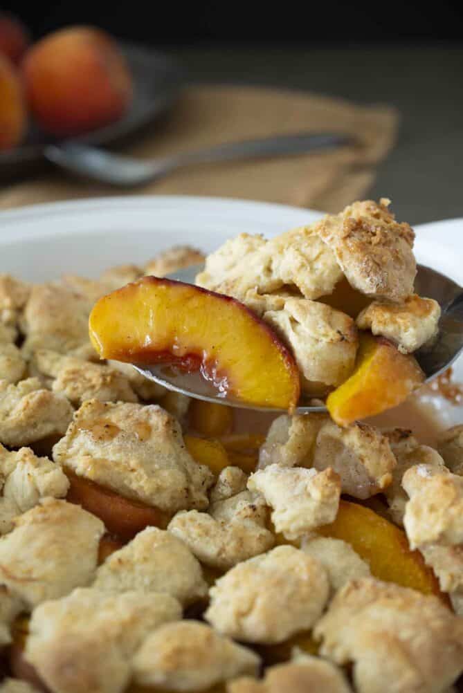 A ladle of sliced peaches and cobbler pastry topping