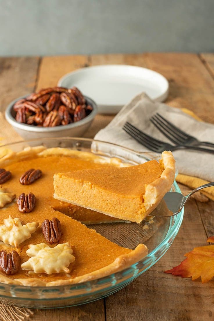 A slice of pie being served with forks and plates and extra maple glazed pecans