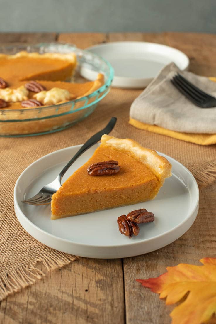 A slice of pie on a white plate with a fork and pecans