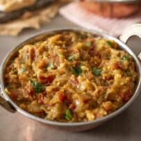 A round copper bowl with handles filled with mashed Indian eggplant and cilantro