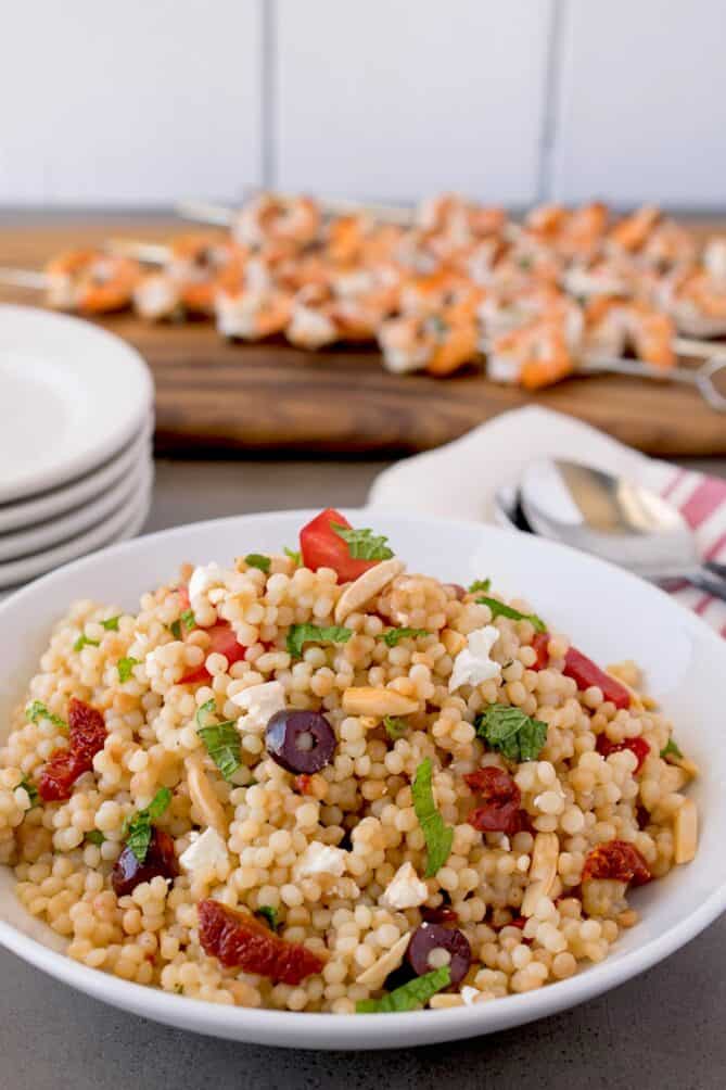 A colorful bowl of couscous with skewers of shrimp in background