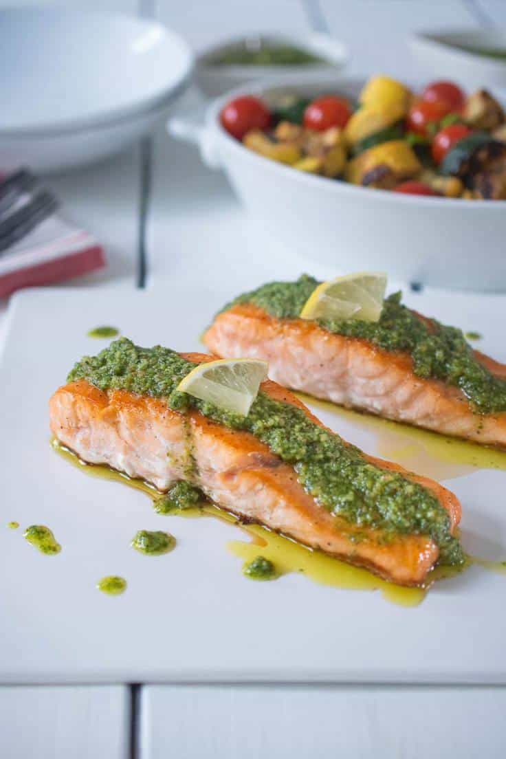 2 salmon filets on a white plate with pesto and lemon