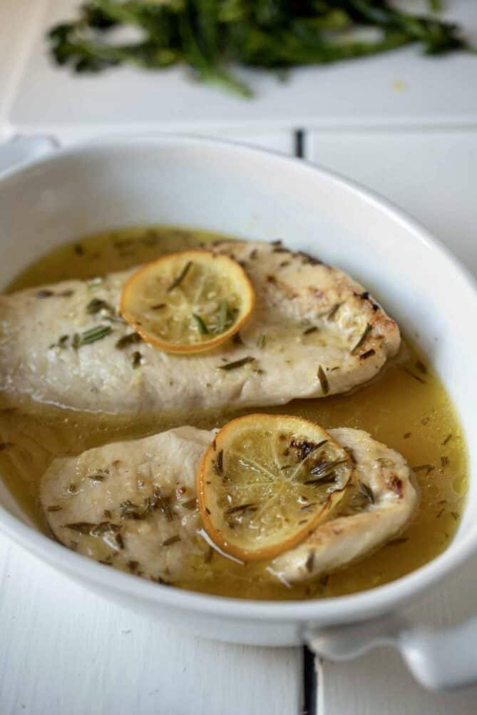 2 chicken breasts in an oval dish bathed in Meyer lemon marinade with slices of lemon