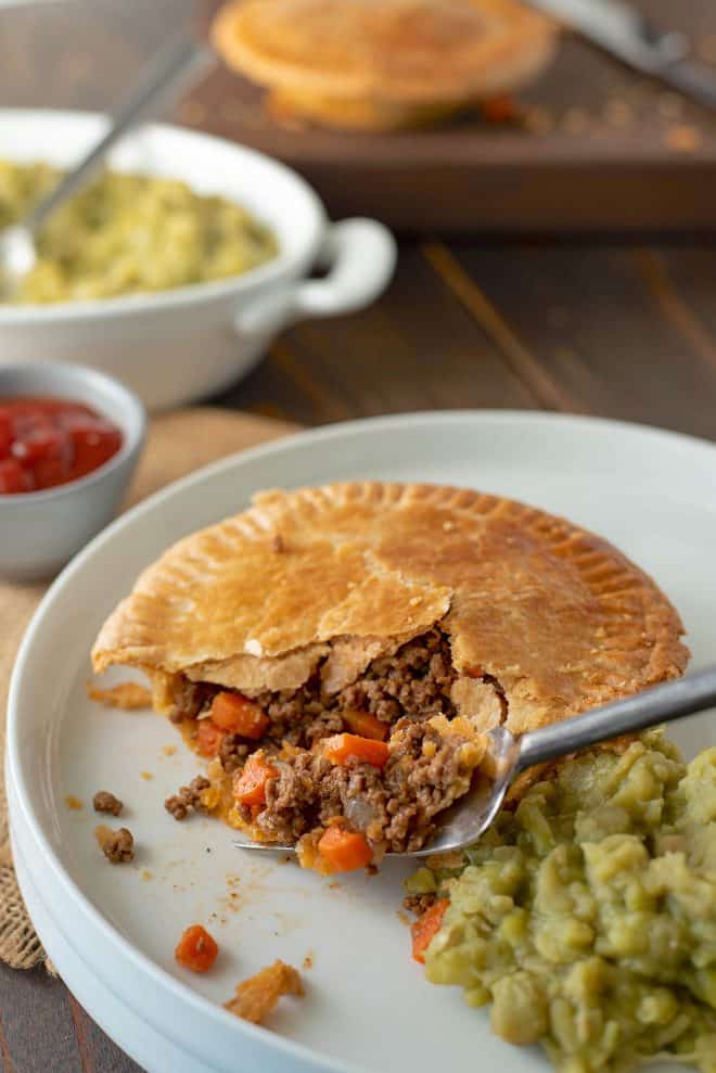 The pie on a white plate with a fork and mushy peas
