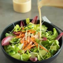 Pouring miso dressing onto a bowl of salad greens and vegetables