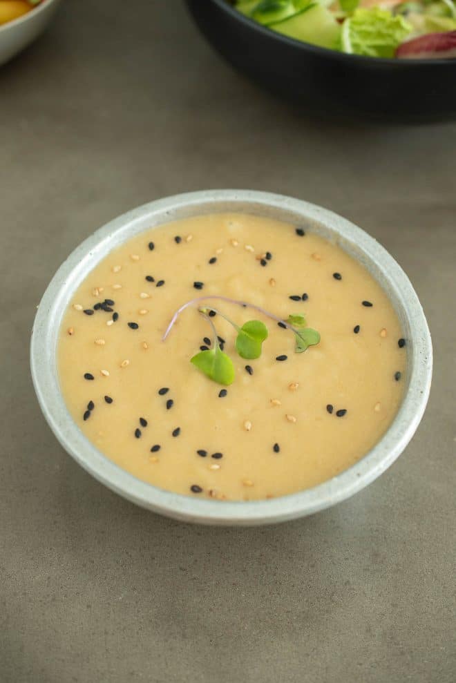 A grey bowl of miso dressing sauce and marinade topped with micro greens and sesame seeds