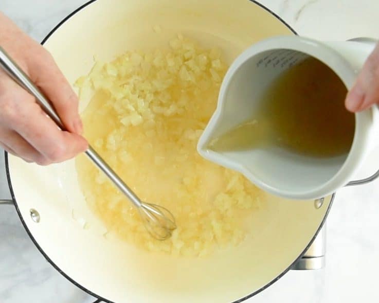 Vegetable stock being poured and whisked into the pan of onions and garlic