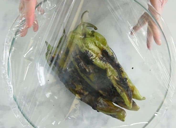 Charred peppers in a glass bowl covered with plastic wrap