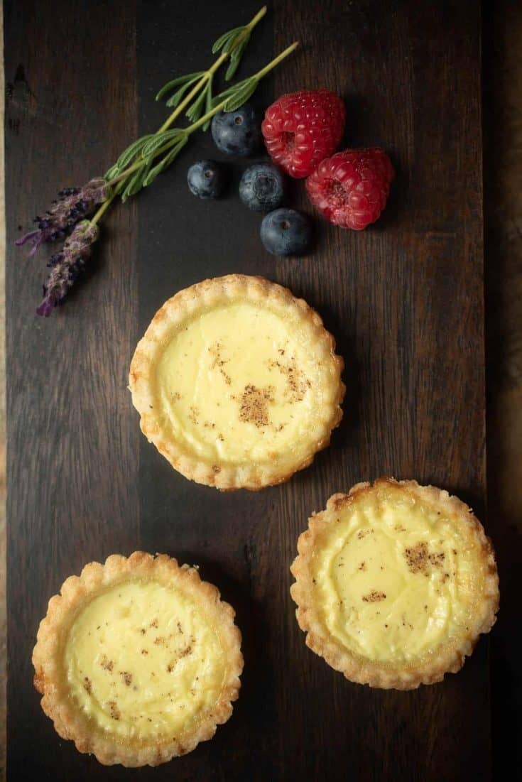 3 egg custard tarts viewed from overhead with fresh lavender flowers, raspberries and blueberries