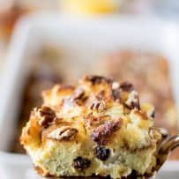 A slice of French toast casserole on a spatula showing the raisins inside and pecans on top