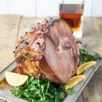 A beautifully glazed ham on a serving tray garnished with orange sliced and parsely
