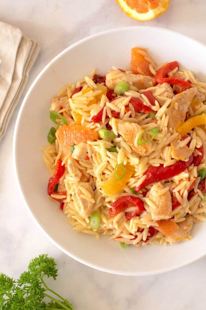 A closeup showing the red peppers, orange segments, chicken and green onions