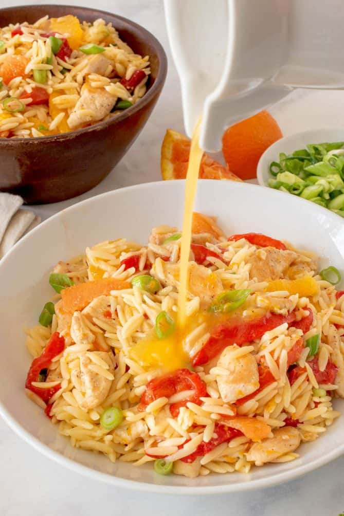 Orzo chicken salad being dressed with orange dressing