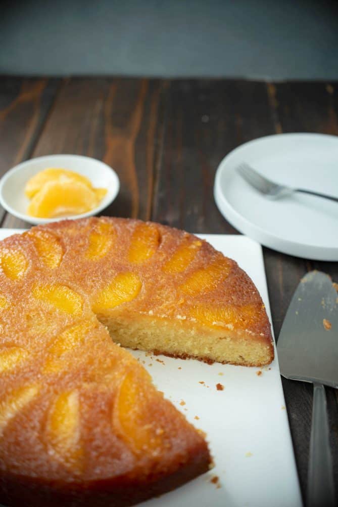 A whole orange salted caramel upside down cake on a square plate with a slice cut out