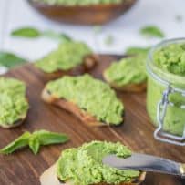Using a knife to spread the pesto on a crusty piece of bread