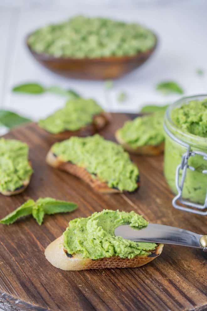 Using a knife to spread the pesto on a crusty piece of bread