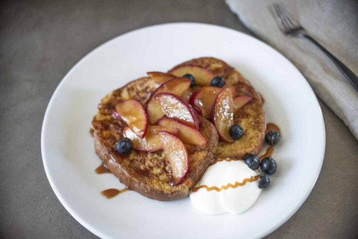 Caramelized peach slices on top of French toast with blueberries and whipped cream