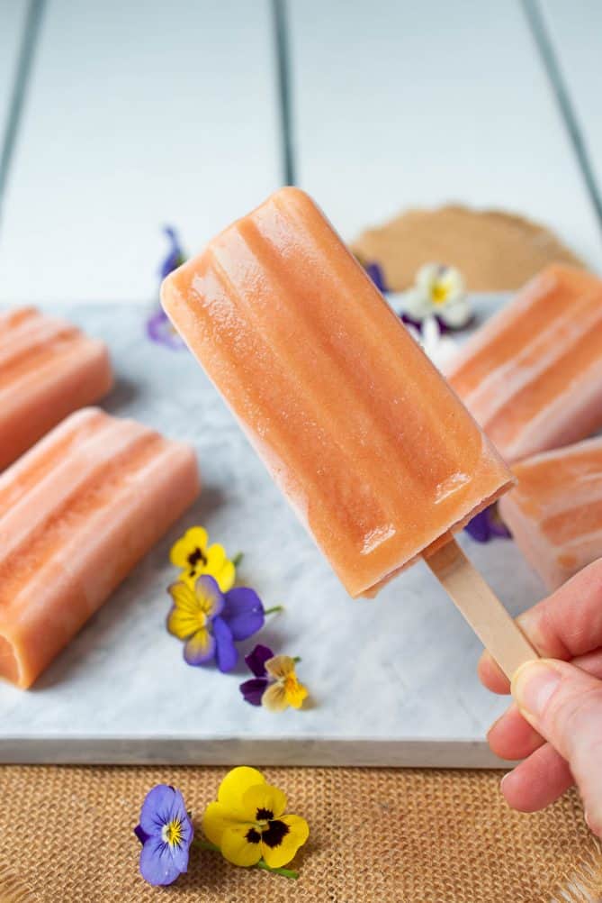 Holding a peach frozen yogurt popsicle with more in the background