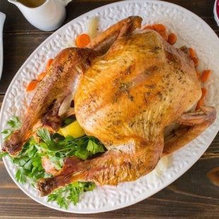 An overhead image of a roast turkey on a white platter with stuffing, mash and cranberry sauce