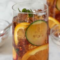 Bronzy hued cocktail garnished with orange, strawberry and fruit slices