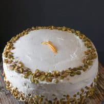 An uncut pistachio cake with orange cream frosting decorated with pistachio pieces