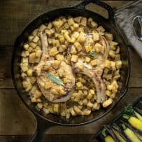 A cast iron skillet with pork chops on a bed of apple salsa
