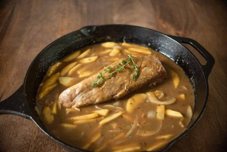 A cast iron skillet with apple and ale gravy and pork tenderloin