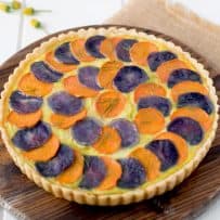 Layers of sliced orange and purple potatoes on top of a quiche