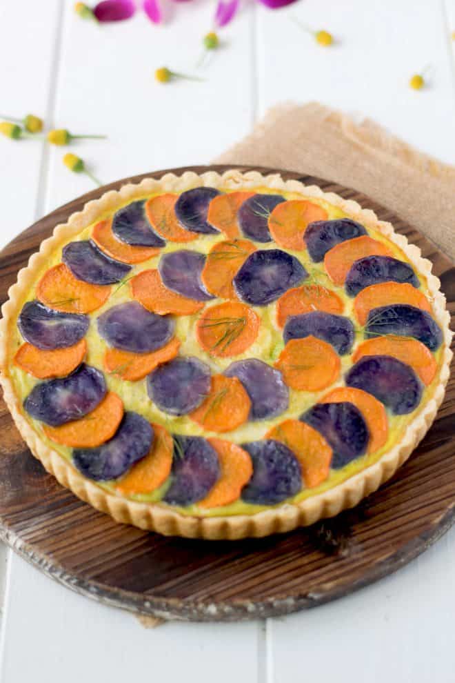 Layers of sliced orange and purple potatoes on top of a quiche
